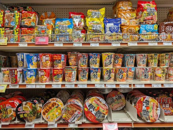 Shelves stocked with various instant noodle cups and snacks